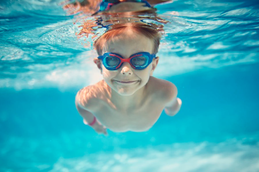 kid swimming underwater with goggles on and smiling